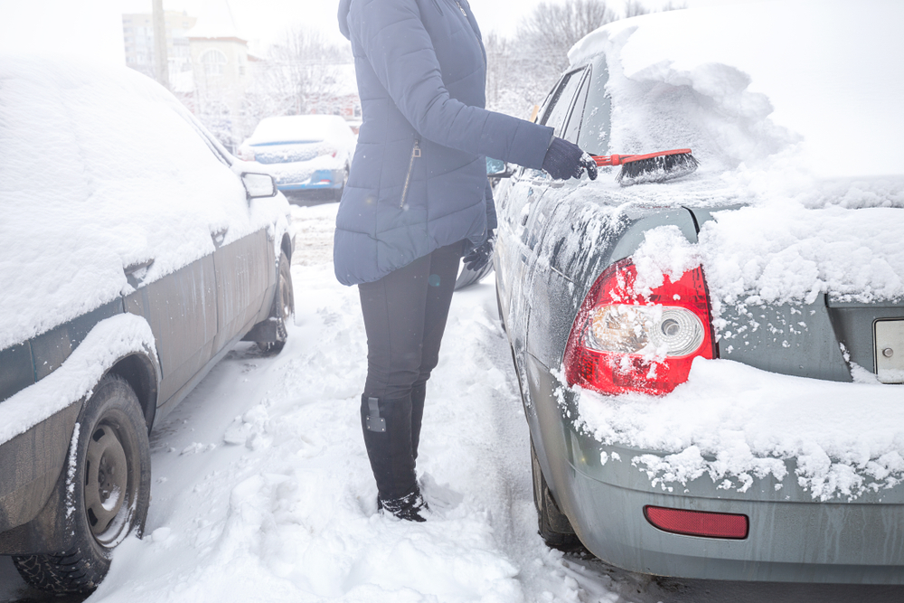 Clearing the snow from the car in the winter in the yard with a shovel, brush and scraper