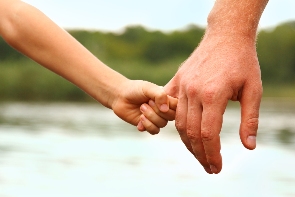 father's hand lead his child son against summer forest and river nature outdoor background