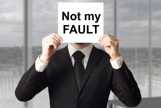 Man holding a sign over his face that says "Not My Fault"
