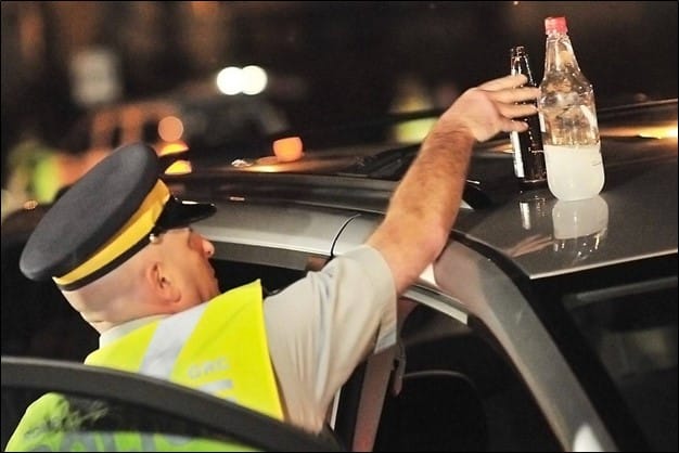A cop pulling open containers of alcohol out of a car.