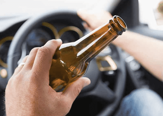 man drinking beer while at the wheel of a car