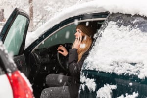 Young woman calling for help or assistance inside snow covered car. Engine start in frost. Breakdown services in the winter
