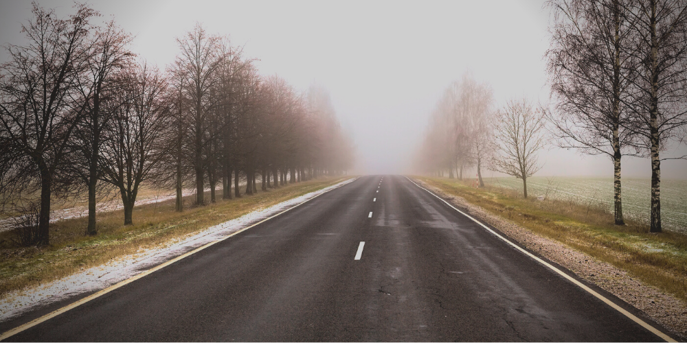 A foggy country road with light snow fall